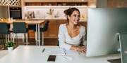 Een vrolijke vrouw die thuis aan het werk is achter de computer met op de achtergrond de keuken en eettafel