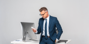 Zakenman leunt tegen bureau aan met een telefoon in zijn hand