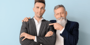 Portrait van senior zakenman die wijst naar zijn volwassen zoon op een blauwe achtergrond