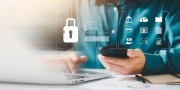 Cyberveiligheid, man achter een laptop met een telefoon in zijn hand