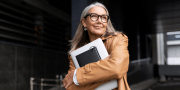 Een dame met bril staat buiten kantoor met een laptop in haar handen