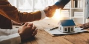 De koopovereenkomst is akkoord. 2 mensen schudden elkaar de hand met op de voorgrond een modelwoning.